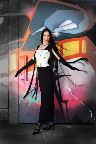 Model mit langem, dunklen Haar vor einer Graffitiwand, sie trägt ein außergewöhnliches und schönes Kleid