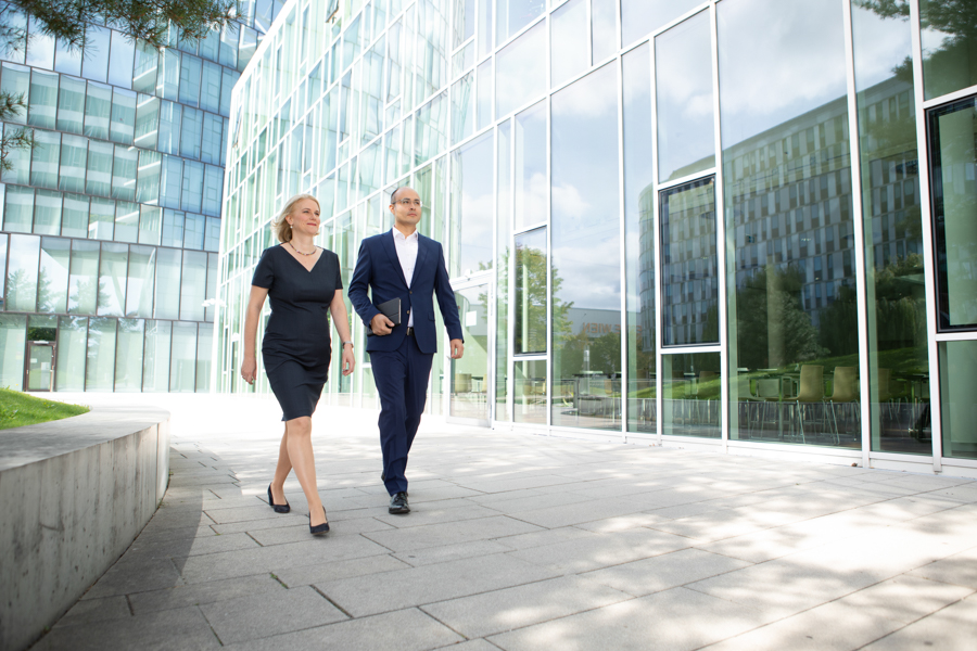 2 Rechtsanwälte, Frau und Mann gehen vor einer modernen Glasfassade