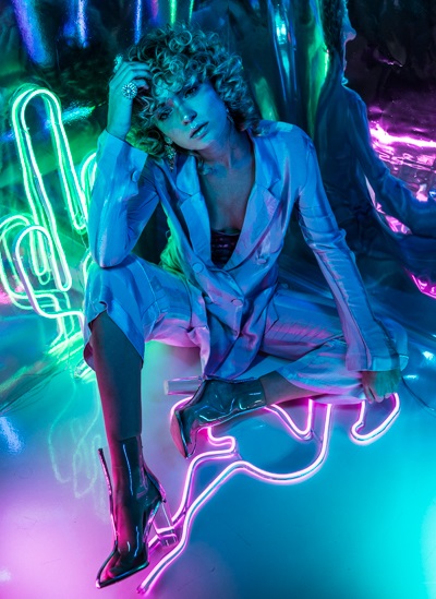High Fashion Photo, schönes blondes Model im stylischen Hosenanzug, buntes Licht, Hologramm-Hintergrund, leuchtende Neonröhren